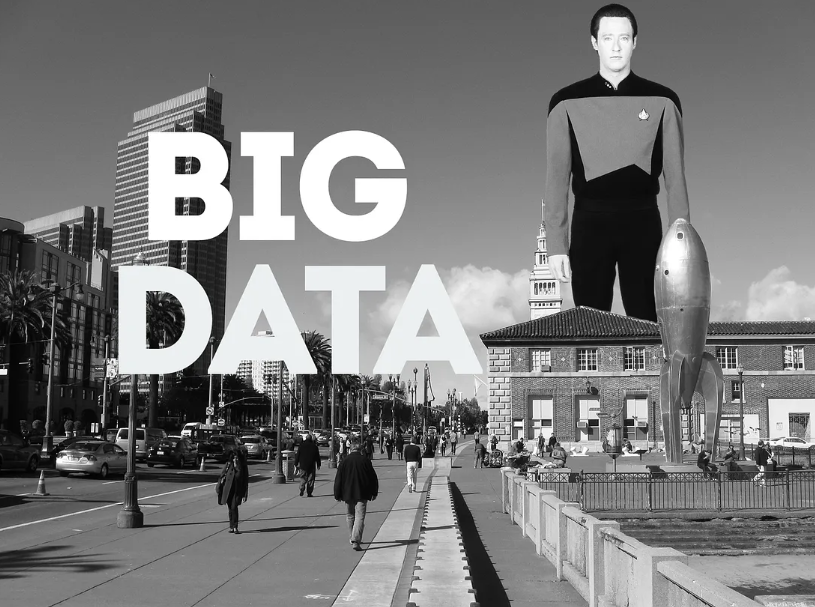 a black and white photo of people walking in front of Pier 14 on San Francisco's Embarcadero, with the "Raygun Gothic Rocketship" sculpture visible (dating the photo to sometime in 2010 or 2011). A giant Lt. Cmdr. Data (Brent Spiner) stands between the Ferry Building and the Ferry Station Post Office Building, taller than the former's clocktower. The large text "BIG DATA" is overlaid on the left side of the image.