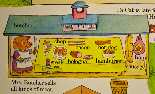 An image from a Busytown book depicting a smiling pig with a knife posing with many meat products including ham and bacon.  It is captioned "Mrs. Butcher sells all kinds of meat."