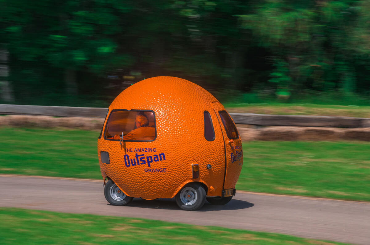 A bright orange car shaped like an orange, belting around a track at almost certainly dangerous speeds.